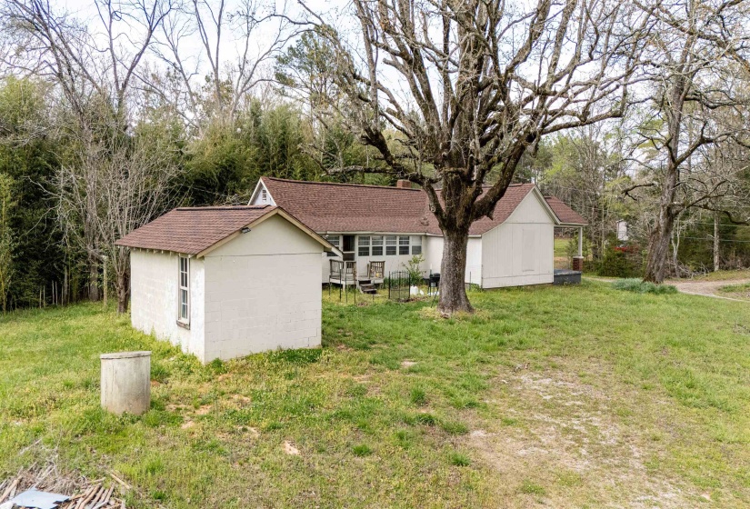 View of front facade featuring concrete block siding, a front lawn, a storage shed, and a shingled roof