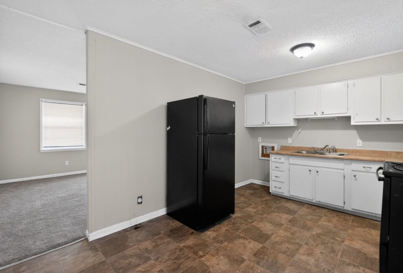 Kitchen with black appliances, white cabinetry, light countertops, a textured ceiling, and stone finish flooring