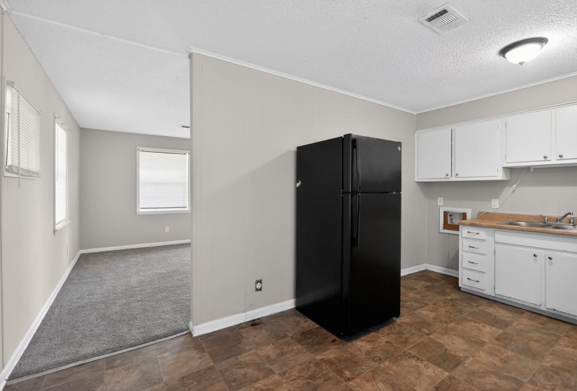 Kitchen with freestanding refrigerator, white cabinetry, stone finish floors, a textured ceiling, and light countertops