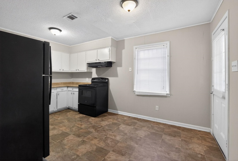 Kitchen featuring black appliances, ornamental molding, white cabinets, light countertops, and stone finish flooring
