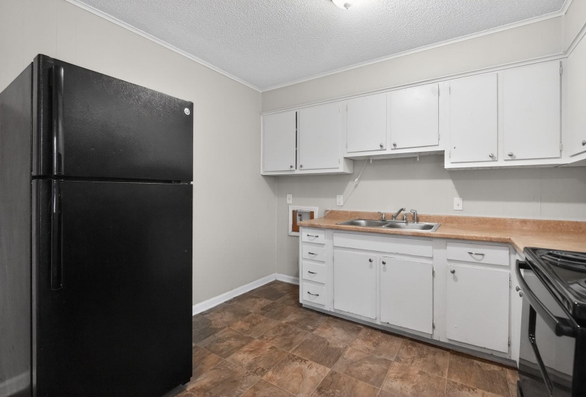 Kitchen featuring black appliances, light countertops, white cabinetry, stone finish flooring, and a textured ceiling