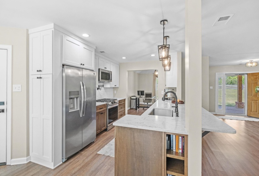 Kitchen featuring light stone counters, stainless steel appliances, a peninsula, light wood-type flooring, and two tone cabinetry