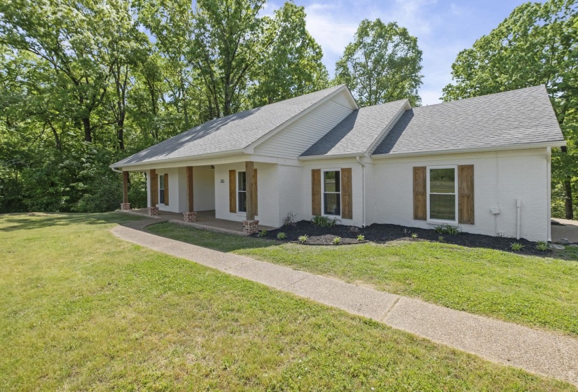 Ranch-style home with a shingled roof, a porch, a front lawn, and brick siding