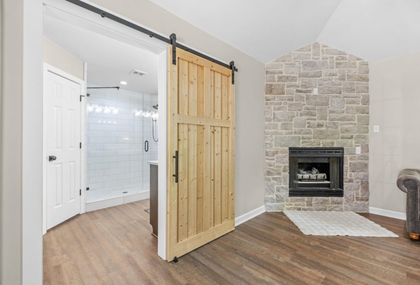 Unfurnished living room with dark wood-style floors, a stone fireplace, vaulted ceiling, and a barn door