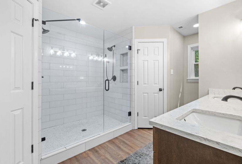 Full bath with double vanity, light wood finished floors, and a shower stall