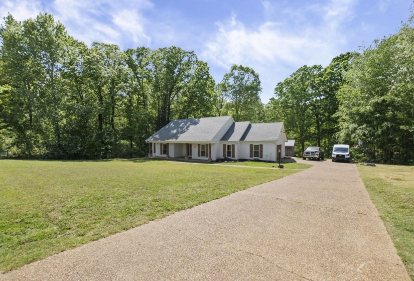 Ranch-style house featuring a front yard, asphalt driveway, and view of wooded area
