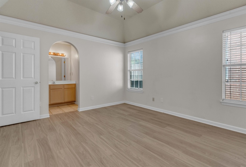Unfurnished bedroom featuring arched walkways, light wood-type flooring, ceiling fan, ornamental molding, and ensuite bathroom