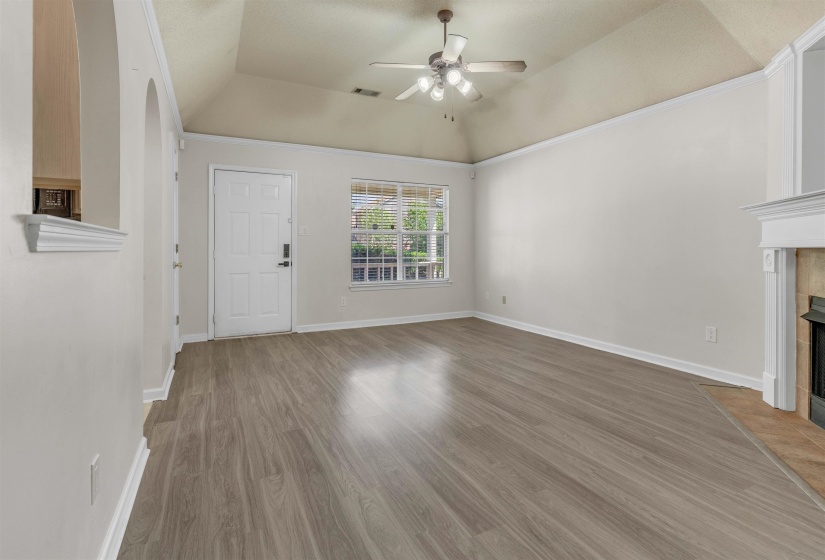 Unfurnished living room featuring a ceiling fan, a tiled fireplace, dark wood finished floors, ornamental molding, and vaulted ceiling