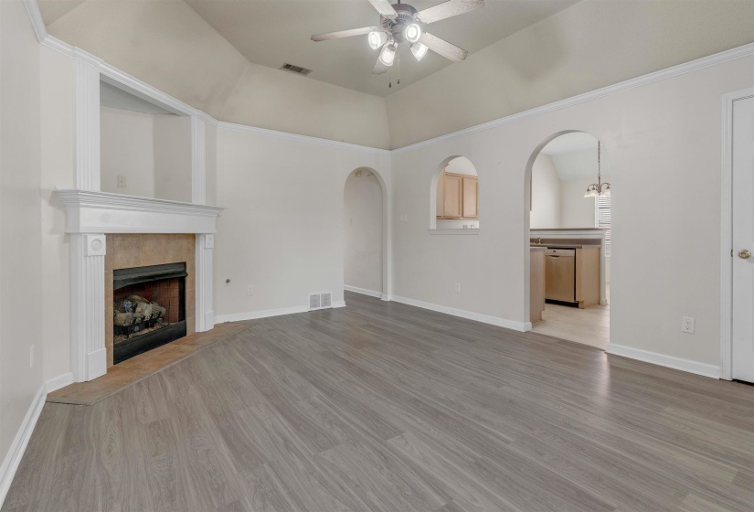 Unfurnished living room with ceiling fan, arched walkways, light wood-style flooring, and a tile fireplace