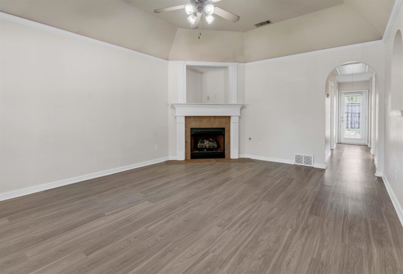 Unfurnished living room featuring ceiling fan, dark wood finished floors, arched walkways, a fireplace, and vaulted ceiling