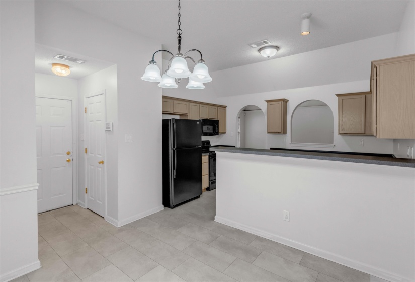 Kitchen with black appliances, dark countertops, hanging lights, and arched walkways