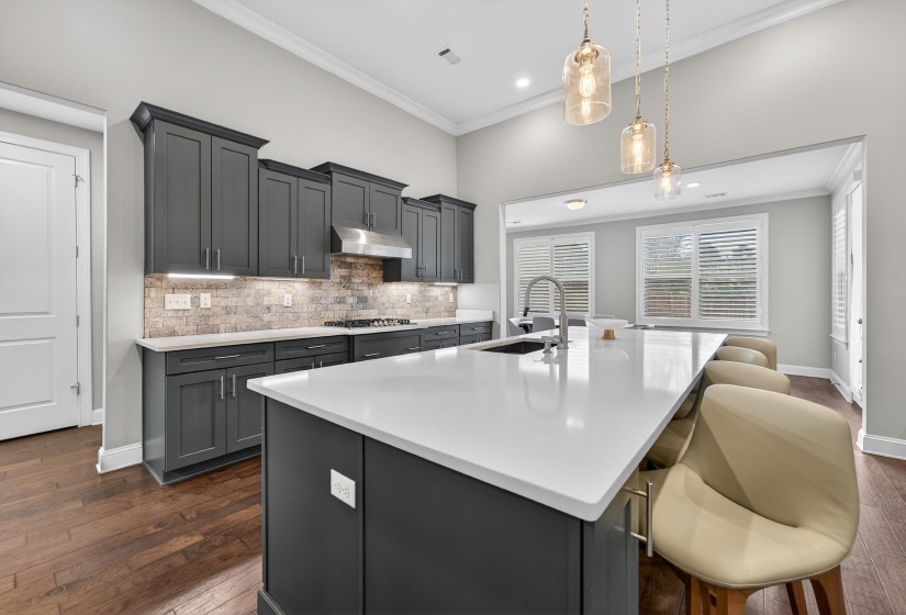 Kitchen featuring an island with sink, dark wood-style flooring, decorative backsplash, a kitchen bar, and light stone countertops