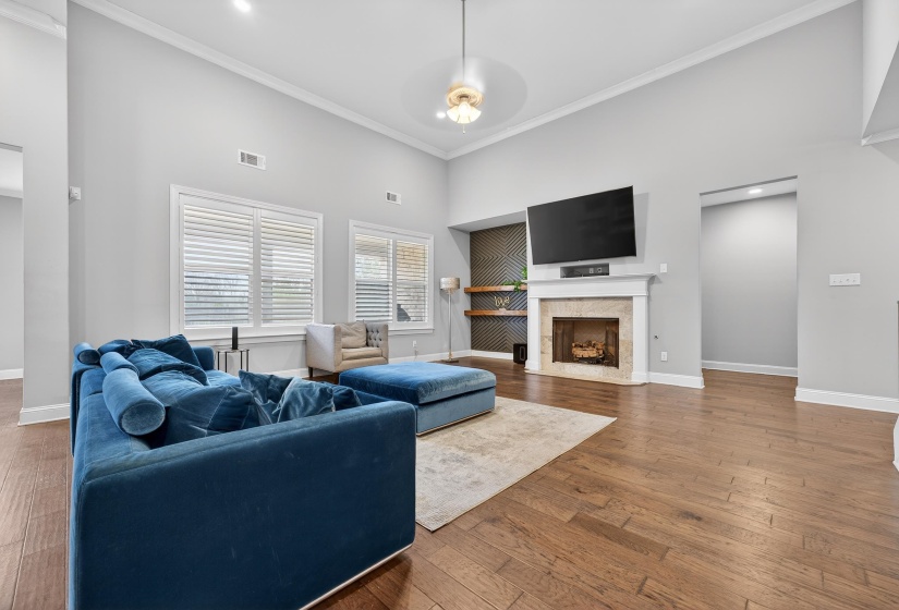 Living room with a high ceiling, hardwood / wood-style flooring, crown molding, a fireplace, and recessed lighting