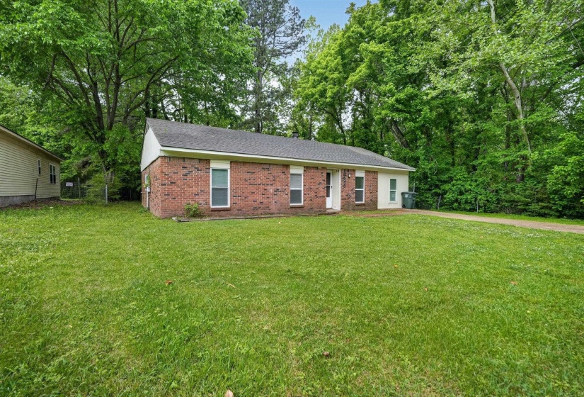 Ranch-style home with brick siding, a front yard, roof with shingles, and view of scattered trees
