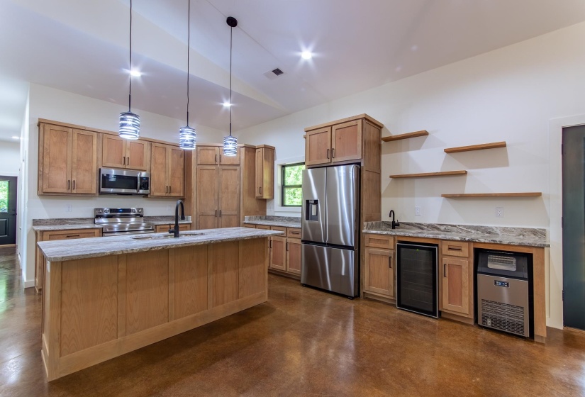 Kitchen featuring light stone counters, finished concrete floors, beverage cooler, stainless steel appliances, and lofted ceiling
