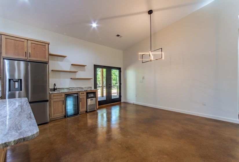 Kitchen featuring concrete flooring, light stone countertops, stainless steel fridge with ice dispenser, open shelves, and beverage cooler