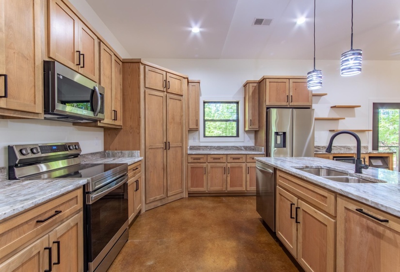 Kitchen featuring stainless steel appliances, light stone counters, finished concrete flooring, hanging light fixtures, and open shelves