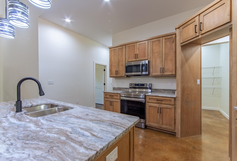 Kitchen with stainless steel appliances, light stone counters, finished concrete floors, pendant lighting, and wood finish cabinets