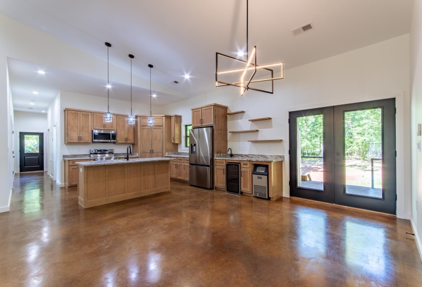 Kitchen with concrete flooring, beverage cooler, a center island with sink, stainless steel appliances, and light stone counters