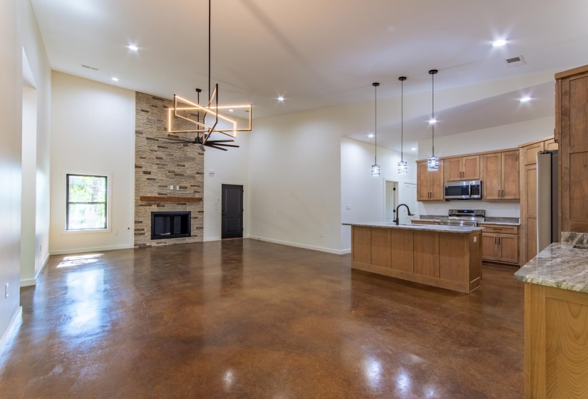 Kitchen with open floor plan, concrete floors, an island with sink, stainless steel appliances, and hanging lights