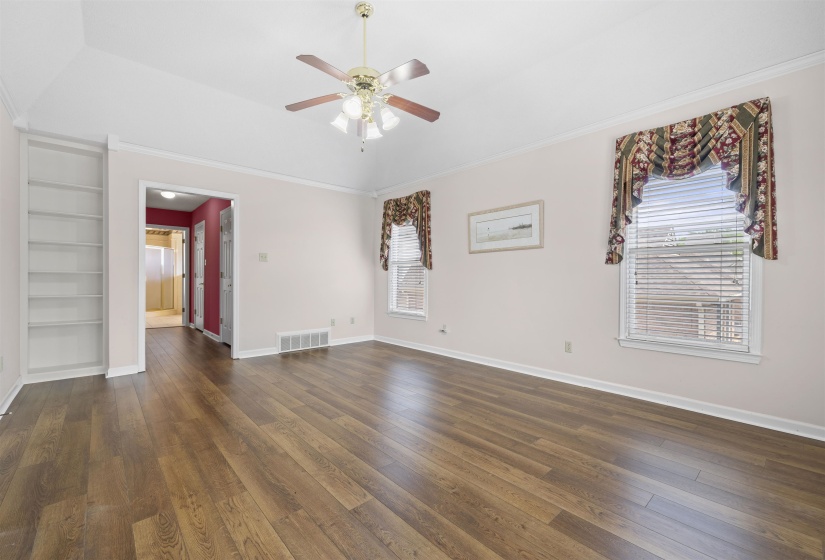 Master Suite with built in features, dark wood-style floors, ceiling fan, healthy amount of natural light, and crown molding