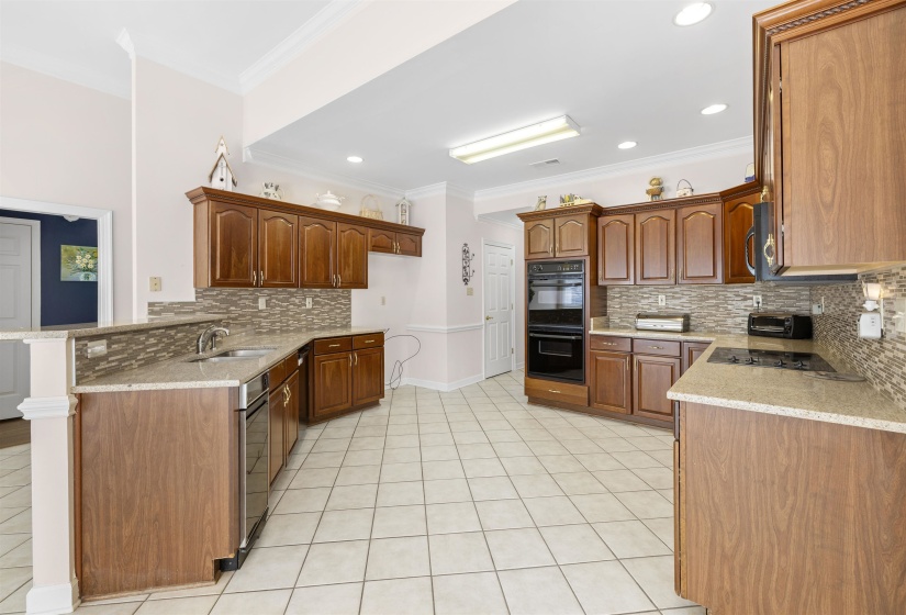 Kitchen featuring a peninsula, crown molding, light stone counters, light tile patterned floors, and wood finish cabinets