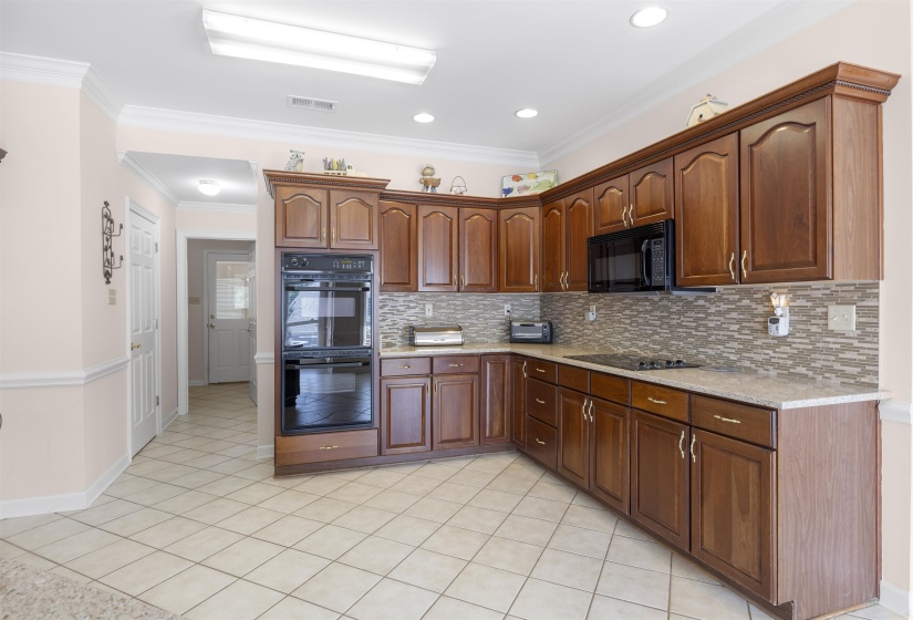 Kitchen with black appliances, ornamental molding, light stone countertops, light tile patterned flooring, and tasteful backsplash