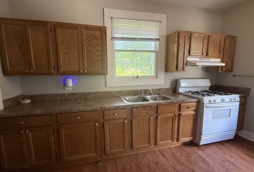 Kitchen featuring white range with gas cooktop, dark wood-type flooring, under cabinet range hood, and brown cabinetry
