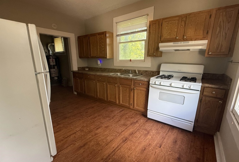 Kitchen featuring white appliances, dark wood-style floors, brown cabinetry, under cabinet range hood, and a textured ceiling