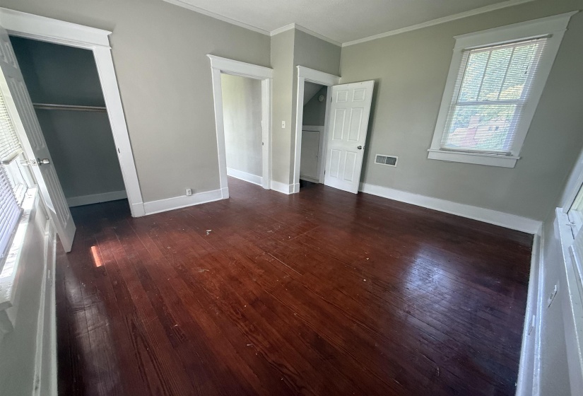 Unfurnished bedroom featuring dark wood-style floors, ornamental molding, and a closet