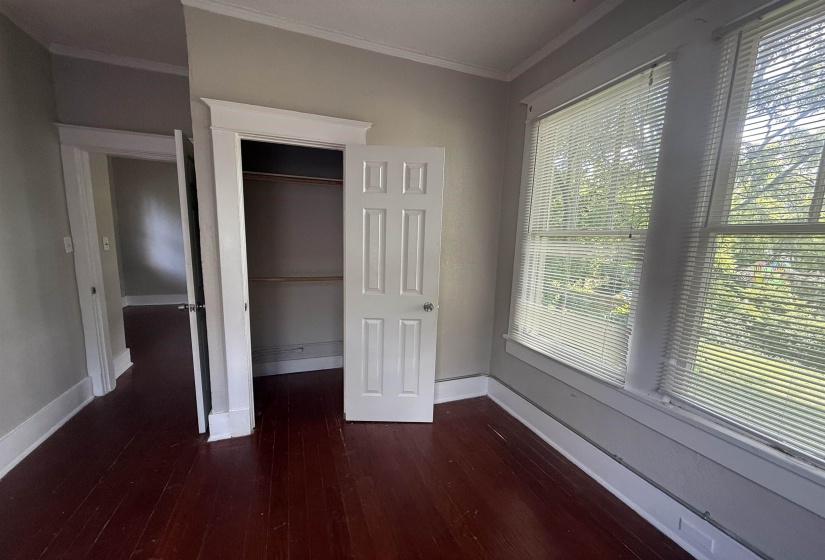 Unfurnished bedroom with dark wood-style flooring, crown molding, and a closet