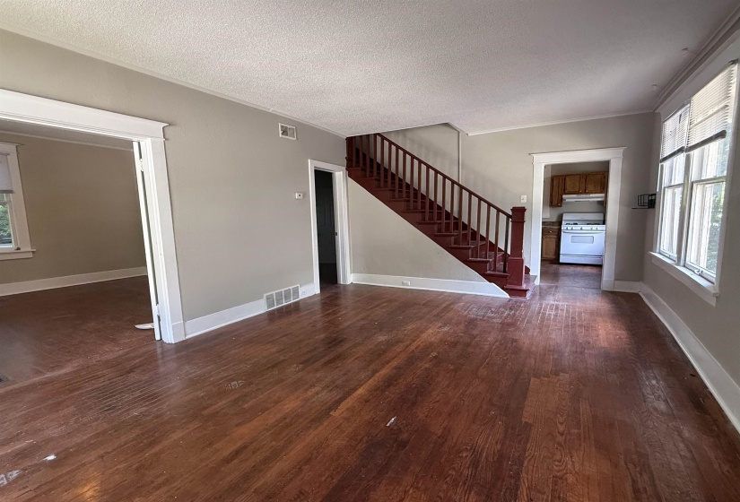 Unfurnished living room featuring dark wood-style flooring, stairway, a textured ceiling, and ornamental molding