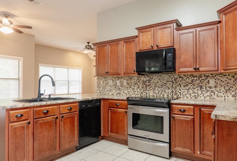 Kitchen with black appliances, a peninsula, light countertops, wood finish cabinetry, and decorative backsplash