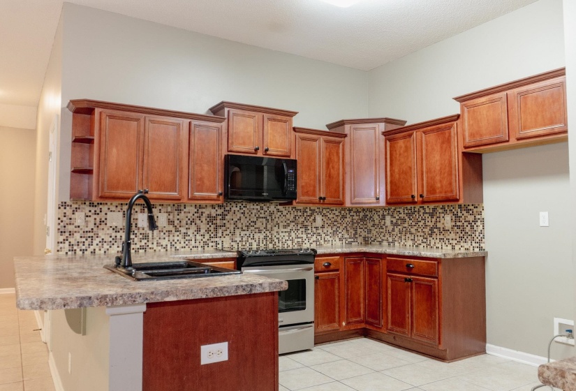 Kitchen featuring stainless steel range with electric cooktop, black microwave, wood finish cabinetry, a peninsula, and open shelves