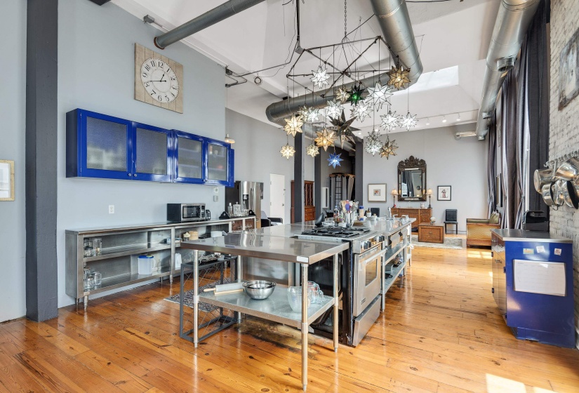 Kitchen featuring a high ceiling, light wood-style floors, stainless steel range with gas stovetop, glass fronted cabinets, and stainless steel counters