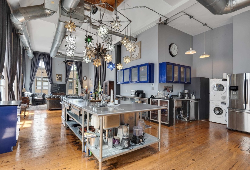Kitchen with stainless steel counters, glass fronted cabinets, stainless steel refrigerator with ice dispenser, a high ceiling, and light wood-type flooring