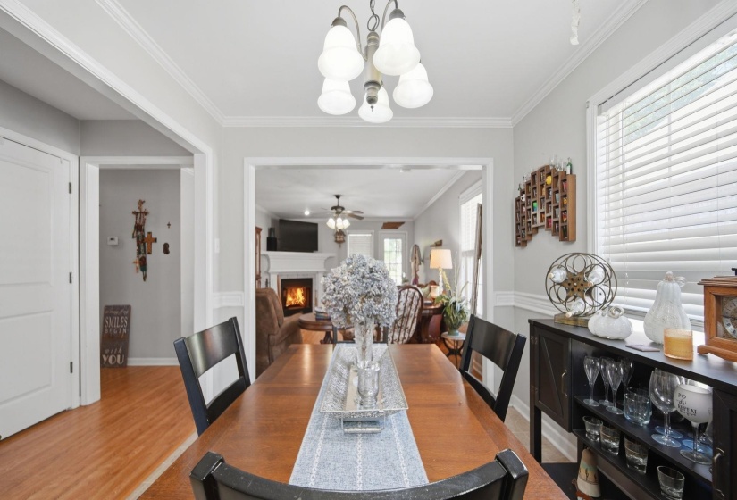 Dining space featuring a lit fireplace, ornamental molding, a ceiling fan, wood finished floors, and suspended lighting