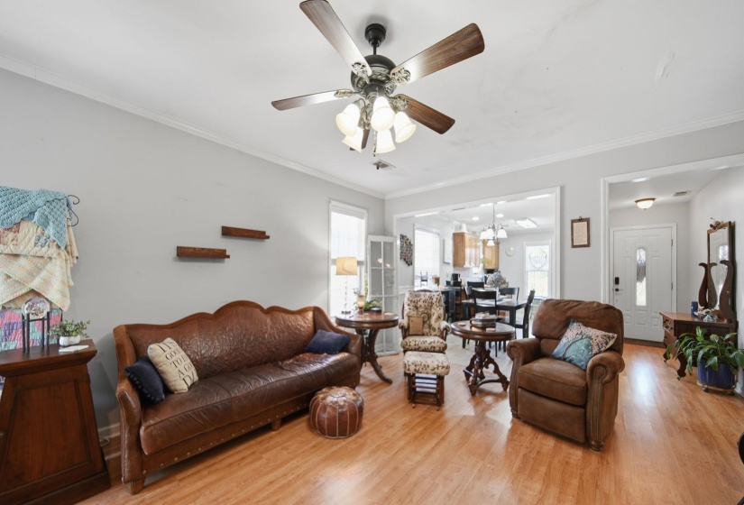 Living area with light wood-type flooring, crown molding, suspended lighting, and a ceiling fan