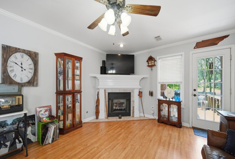 Living room with light wood-style floors, crown molding, a ceiling fan, and a tiled fireplace