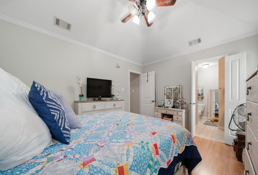 Bedroom with vaulted ceiling, ornamental molding, light wood finished floors, and a ceiling fan