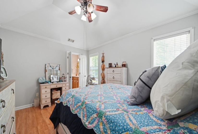 Bedroom with multiple windows, ornamental molding, lofted ceiling, light wood-style flooring, and a ceiling fan