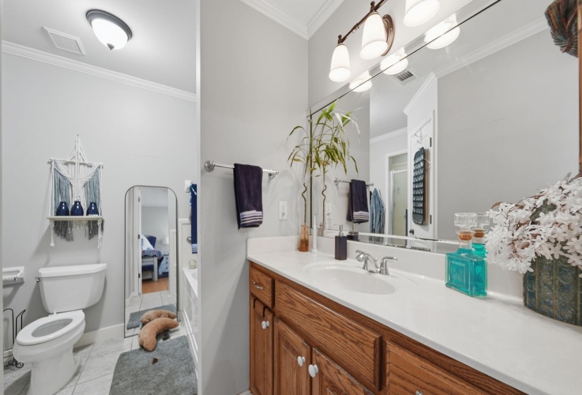 Ensuite bathroom with crown molding, vanity, light tile patterned floors, and a garden tub