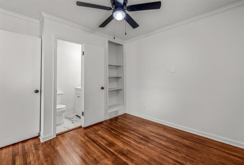 Unfurnished bedroom with ornamental molding, dark wood-type flooring, a ceiling fan, and ensuite bathroom