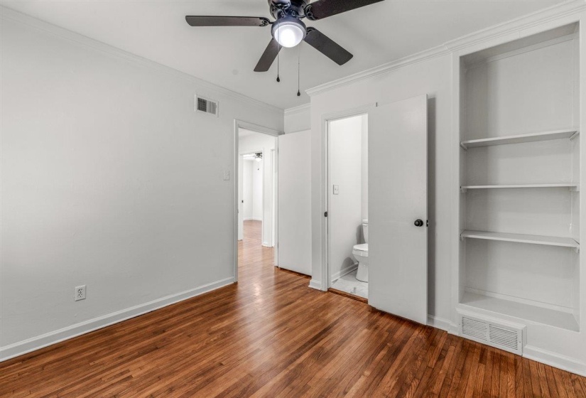 Unfurnished bedroom with crown molding, dark wood-type flooring, a ceiling fan, and ensuite bath