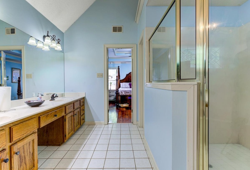 Ensuite bathroom with double vanity, a stall shower, light tile patterned floors, and hanging lights