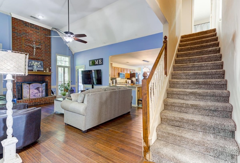 Living room featuring a fireplace, dark wood-type flooring, vaulted ceiling, a ceiling fan, and a chandelier