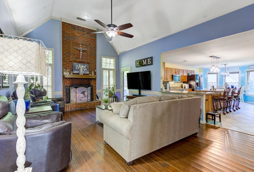 Living room with a ceiling fan, crown molding, light wood finished floors, a high ceiling, and a fireplace