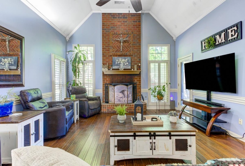 Living area with ornamental molding, a ceiling fan, a fireplace, dark wood finished floors, and a high ceiling