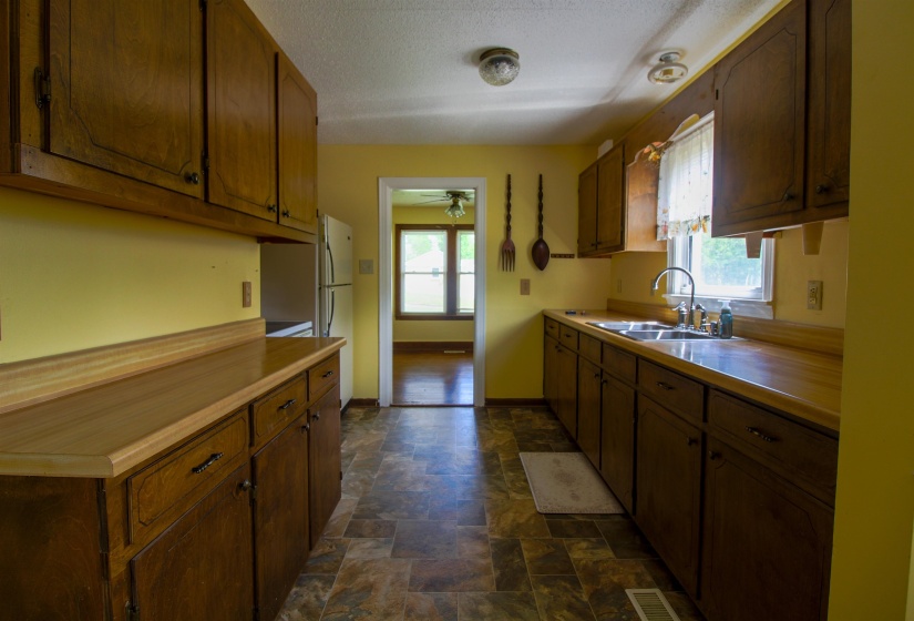 Kitchen with stone finish flooring, light countertops, a textured ceiling, freestanding refrigerator, and a ceiling fan