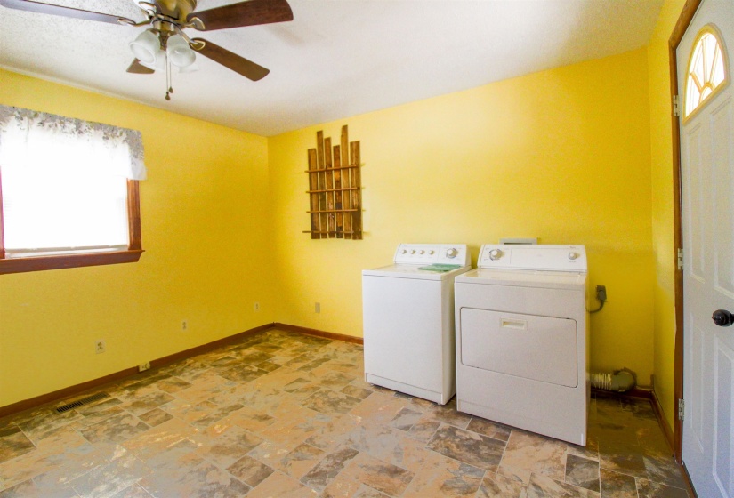 Laundry area featuring healthy amount of natural light, ceiling fan, light stone finish floors, and washer and clothes dryer